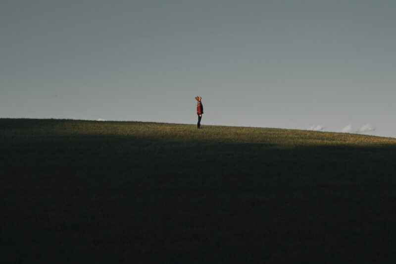 A full-length photo of a lone man on a hill in a red jumper with his head tilted back taking a big deep breath