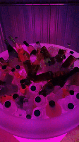 a moving gif showing an Almore pot filled with ice, beers, wines and cans. A hand comes in from the right, picks up a beers and disappears to the right. The plant pot is changing colours the whole time this is happening. 
