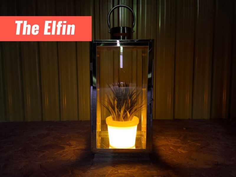 The small, Elfin LED Plant pot in a lantern-style candle holder. The pot is glowing a deep orange colour