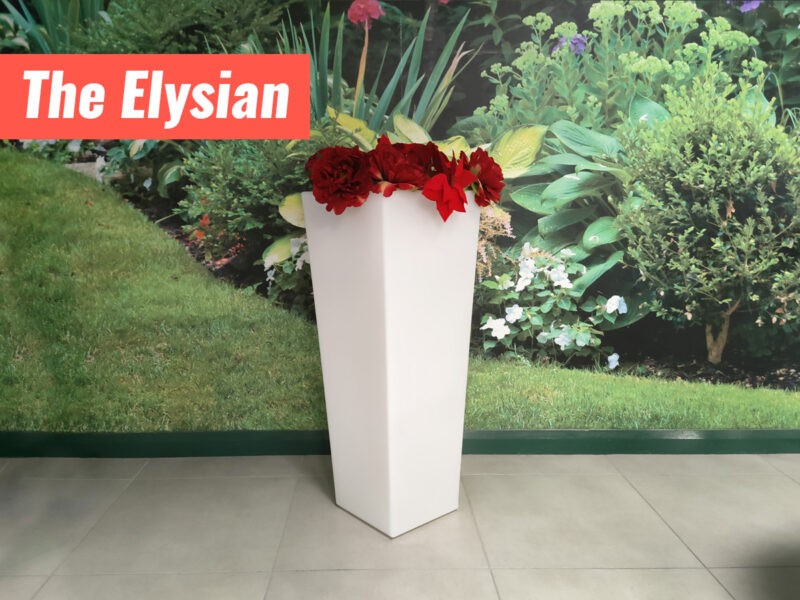The Elysian Plant pot filled with Poinsettia flowers. It is a tall, white flower pot that is about three times as tall as it is wide. It is more narrow at the base than it is at the top.