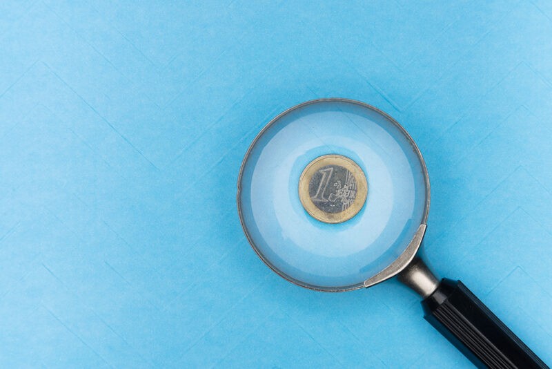 A photo of a euro under a magnifying glass against a blue background