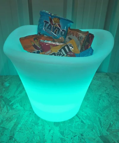 The Petal Flower pot filled with cans of soft drink and crisps. It is glowing teal