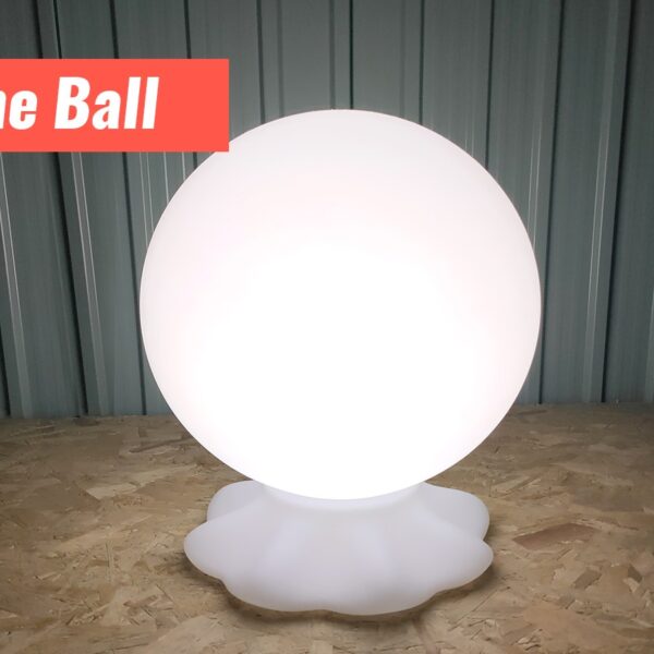 A ball shaped LED light standing on a white faux-rock base. Its on a plywood foundation and against a metal wall