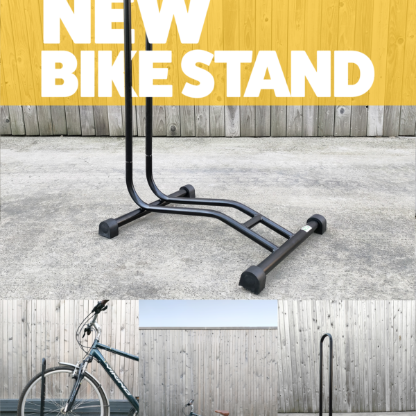 A black bike stand against a great wall and concrete flooring. There is a yellow banner that goes through the hoop of the bike stand with text on it that reads 'bike stand'