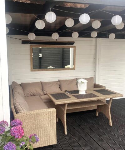 The Ronan Heating heater with speaker mounted on the wall of a pergola. The walls are white, the floor is black and there is bunting-lights hanging from the room. Above a mirror on the wall, the ronan heating is visible