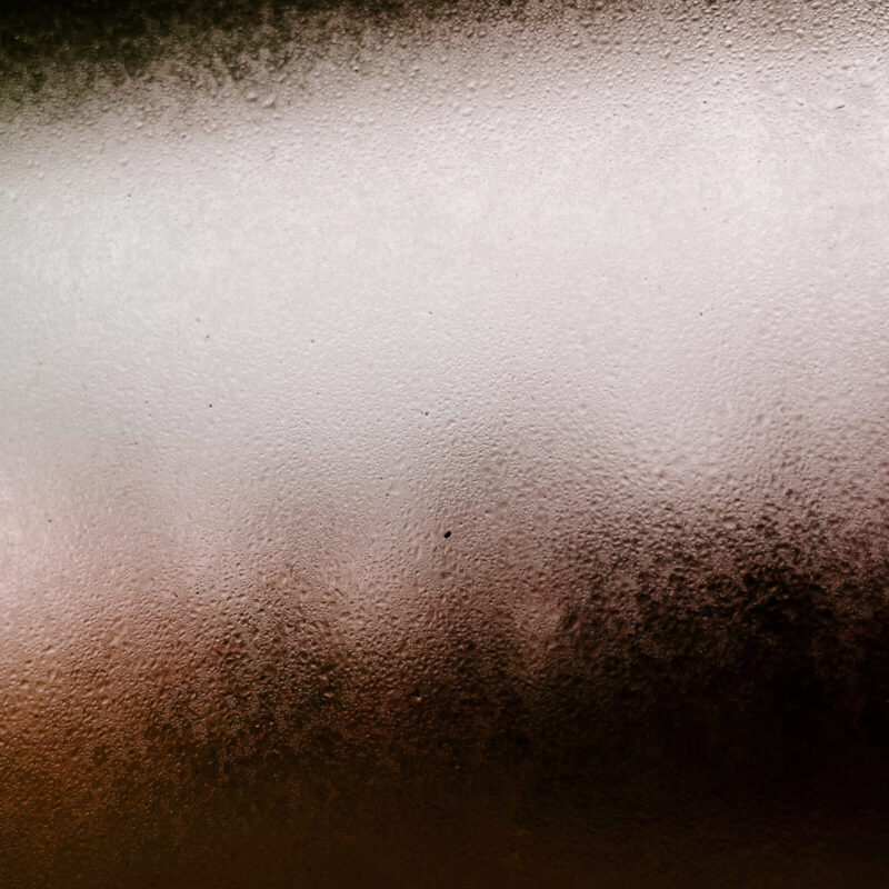 Condensation droplets on a window with a red light backlighting the glass pane