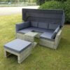 The outdoor rattan garden sofa set from sheds direct Ireland outside on a green lawn. The unit it a rattan, light-brown colour and the cushions and awning are a dark grey colour.