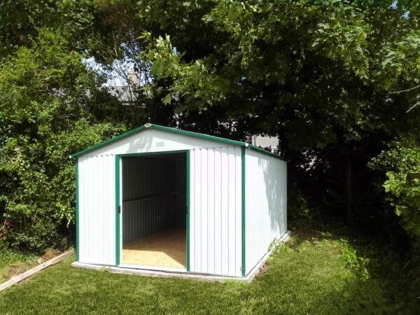 A white-Grey steel garden shed in the corrner or a large garden. Two large trees are behind it, as are large shrubs. The grass is a lush green and the shed is reflecting the sun's rays. The doors of the shed are open and inside the shed is empty.