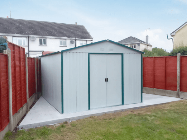 The off-white colossus shed in a triangluar garden with two red fences either side of the shed