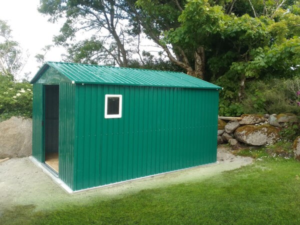 A photo of the colossus shed in a grassy garden. The doors are open, there is a window installed in it and there is large shrubs behind it.
