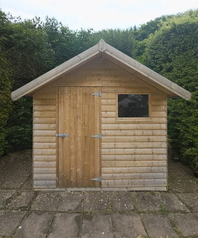 Overhang wooden shed exterior, in front of a bush