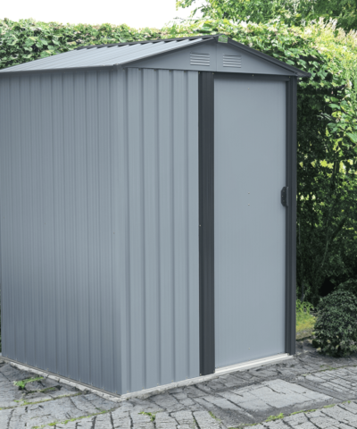 The Tiny Shed in a paved garden, in front of a large bush