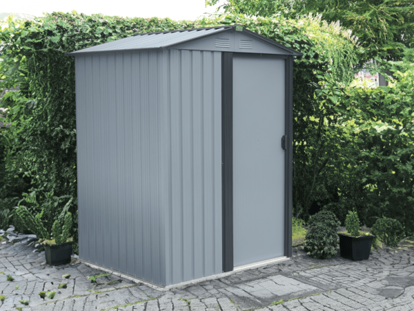 The Tiny Shed in a paved garden, in front of a large bush