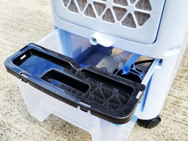 The reservoir is open at the back of the air cooler. The lid is a black plastic, the sides are clear plastic and a semi-clear, blue tinted tube can be seen sucking the water up through the unit