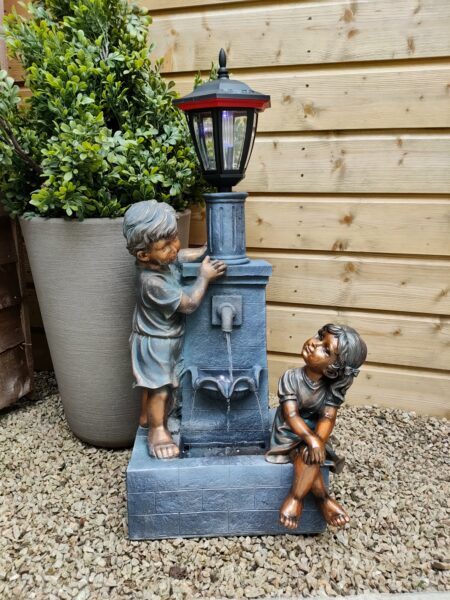 Two bronze children sitting on a plinth with a tap between them pouring water