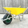 The yellow 90l plastic wheelbarrow against a wooden wall