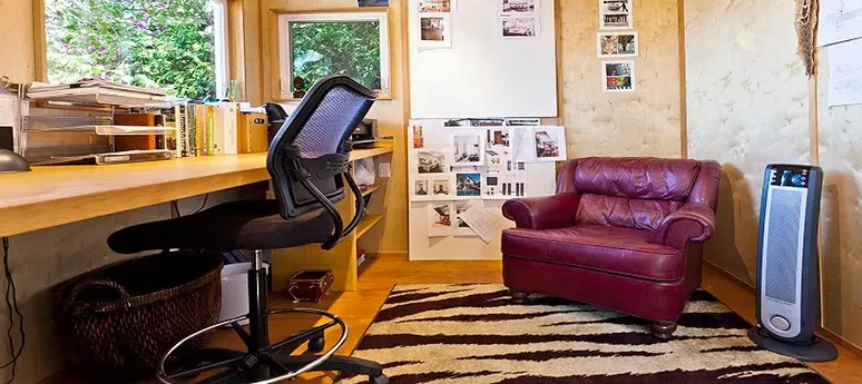 A Shed converted into an office with a couch and a desk placed inside