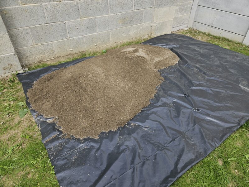 A pile of brown gravel heaped up to the left hand side of a black, damp-proof membrane