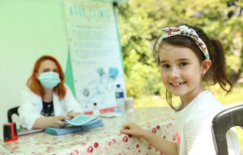 A young girl at a table with a doctor who has a prescription pad and a pile of children's books in front of her