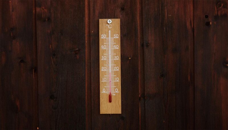 A Light brown thermostat on a dark brown wooden wall