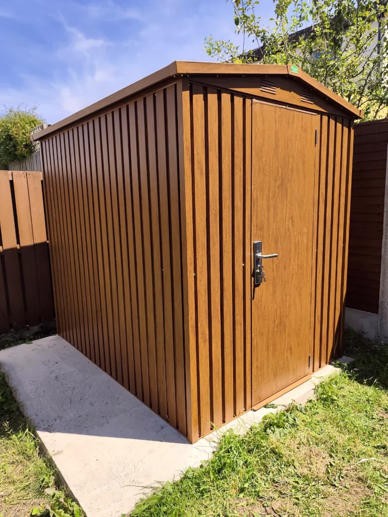 A front-view of the Woodgrain shed with the door closed. It's on a concrete slab in a small garden