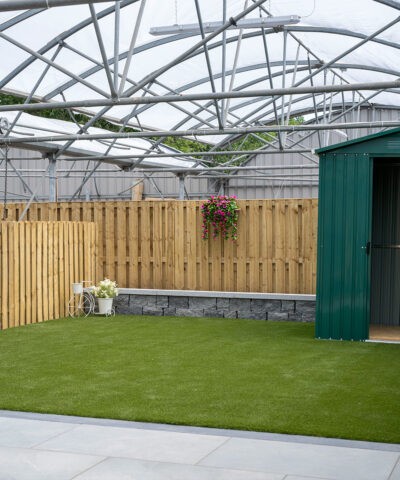 A green garden shed sitting on artificial grass