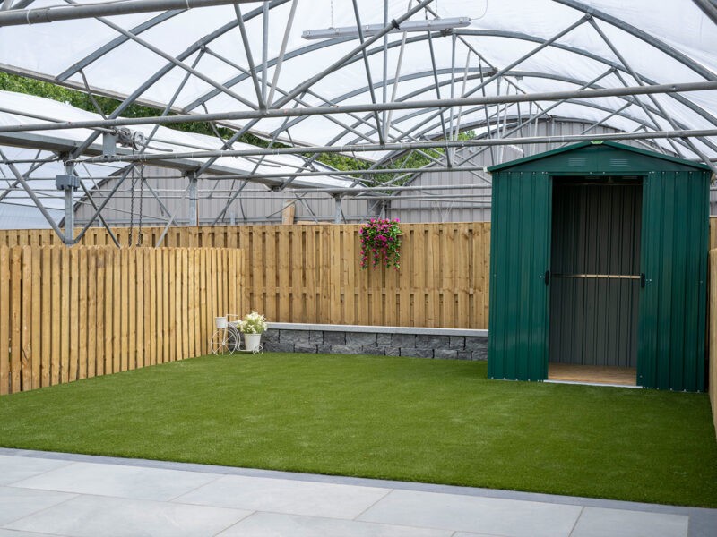 A green garden shed sitting on artificial grass