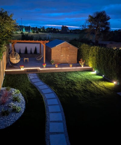 A garden with astroturf at night, lit by lights within the garden