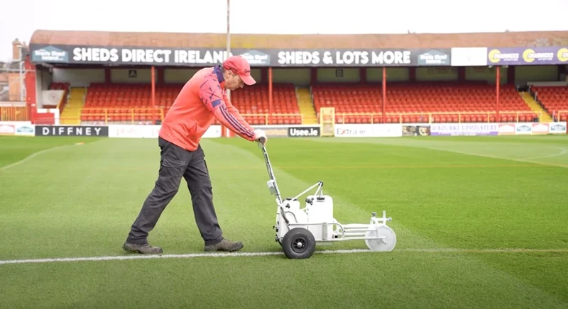 The Shelbourne Groundskeeper making the lines of Tolka Park with the Sheds Direct Ireland advertising boards behind him